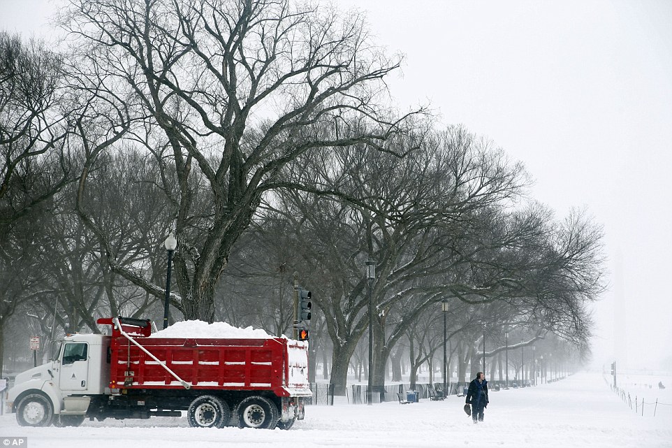 A pedestrian waits to cross the street as a truck carrying a load of snow passes in front on the National Mall in Washington