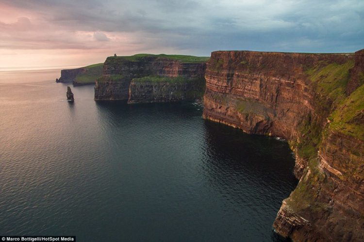As the sunsets over the towering Cliffs of Moher in County Clare (above), Republic of Ireland, the pink light warms the craggy strata of the rockface