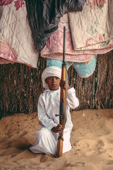A bedouin boy in Oman poses with his father's rifle